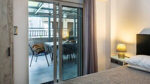 A hotel room with a bed, a nightstand, a lamp, a sliding glass door leading to a balcony with a table and chairs. - GnG Apartment 1 by RentalsPro - Nea Flogita (Nea Flogita)