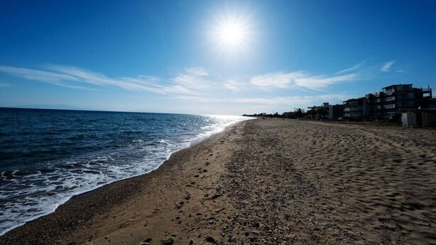 En strand med klar himmel, vågor som slår in mot land och byggnader längs kusten.
