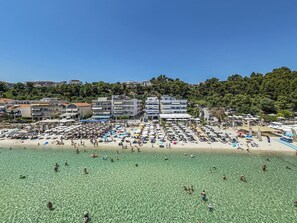 Ein Strand mit klarem Wasser, Sonnenschirmen und Gebäuden im Hintergrund.