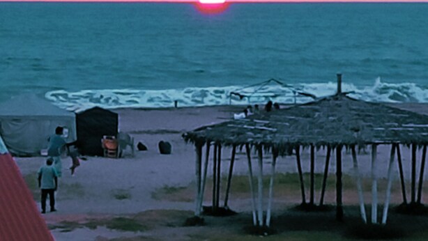 A sunset over the ocean with a beach and a thatched structure. - Charming 2-bedroom apartment with AC in sunny Playas (Playas)