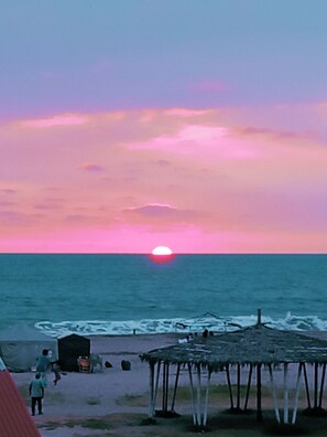 Un coucher de soleil sur l’océan, avec une plage et une structure à toit de chaume.