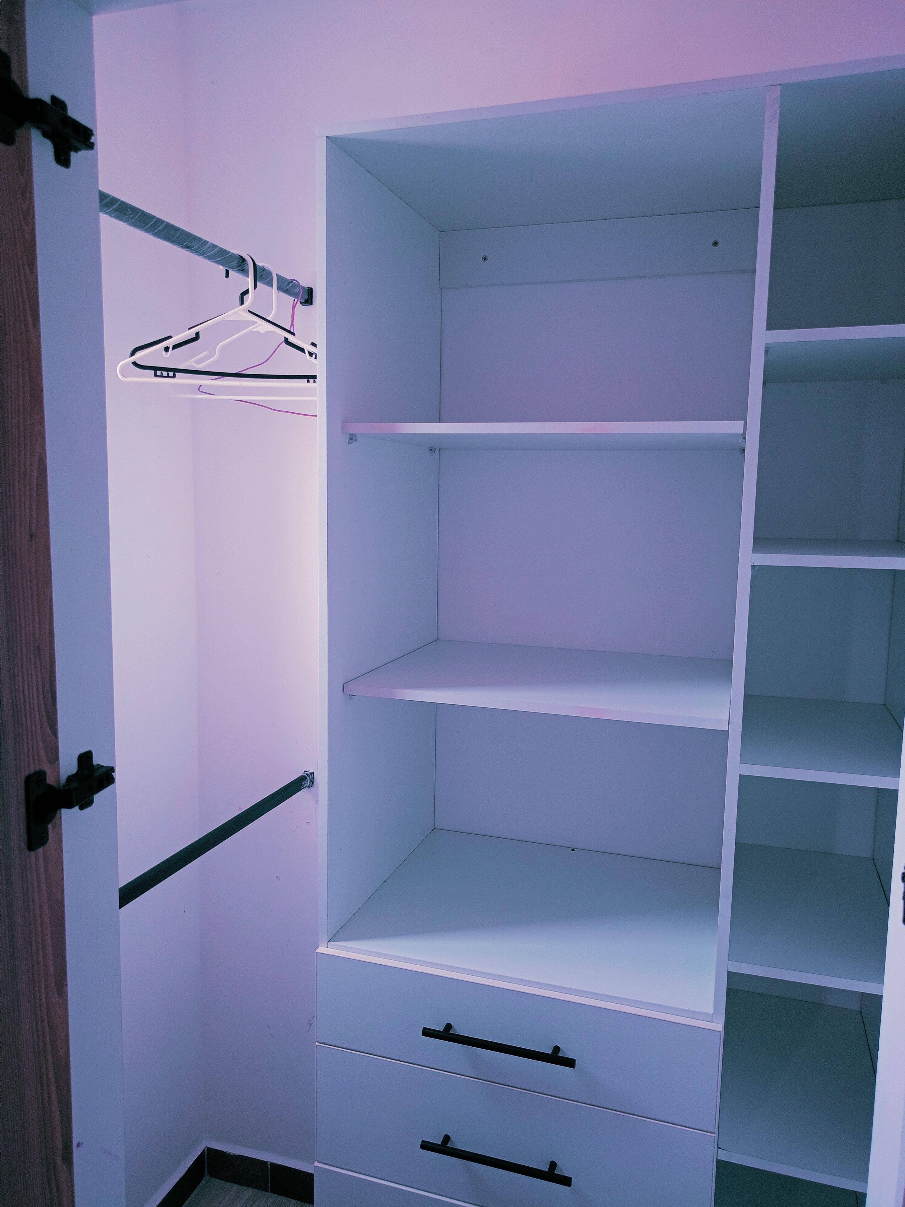 Un dressing accessible sans porte, doté d’étagères ouvertes, d’une tringle et d’une porte avec une poignée.