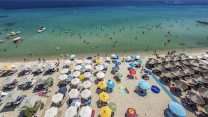 Una spiaggia con molti ombrelloni e lettini, un mare cristallino e imbarcazioni all'orizzonte.