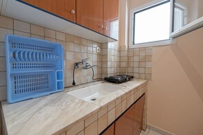 A kitchen with a sink, a blue plastic basket, and a window.