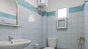 Un baño con lavamanos, inodoro, ducha y un ventanal pequeño.