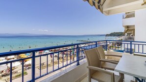 Balcón con mobiliario de mimbre con vista a una playa con gente y barcos.