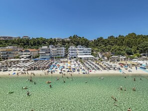 Ein Strand mit klarem Wasser, Sonnenschirmen und Gebäuden im Hintergrund.