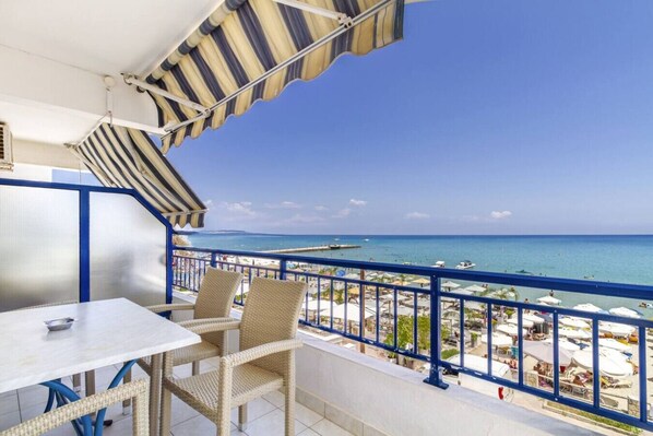 A balcony with a view of the beach, a table, and wicker chairs. - Poseidon Edge No18 by RentalsPro - Kallithea (Kallithea)