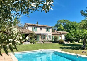 Ein zweistöckiges Haus mit Swimmingpool, umgeben von Grünpflanzen und blauem Himmel.