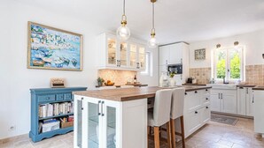 A kitchen with white cabinets, a blue bookshelf, a large island with chairs, pendant lights, and a painting on the wall. - 4-bed 3.5-bath Villa, Pool, Close to Callian- Pays de Fayence (Callian)