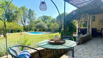 A patio with a table and chairs, a hanging light fixture, a pool, and a garden.