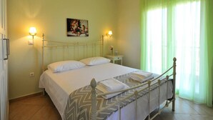 Une chambre à coucher avec un lit, deux lampes de chevet, une table de chevet, un tableau et une fenêtre avec des rideaux légers.