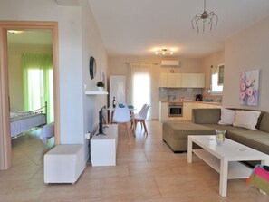 A modern living room with a sofa, coffee table, and a dining area with chairs and a table. - Fotinia Beach House by RentalsPro 1st floor (Paralia Dionisiou)