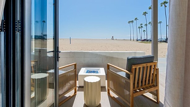 Un balcone con vista sulla spiaggia, sedie di legno, un tavolino e una porta in vetro.