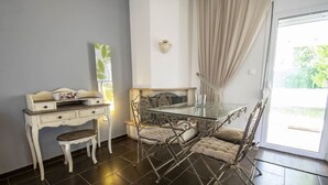 A dining area with a glass table and metal chairs, a white dresser with drawers, and a view through a glass door. - Sunlight  Maisonette by RentalsPro (Nikiti)
