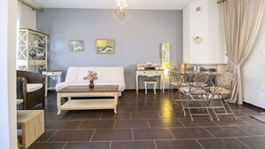 A room with a bed, a desk, a chair, a chandelier, and artwork on the wall. - Sunlight  Maisonette by RentalsPro (Nikiti)