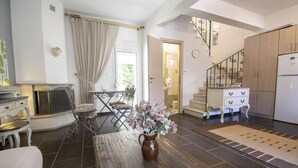 A spacious living area with a dining table, a sofa, a kitchen with a refrigerator, and a staircase. - Sunlight  Maisonette by RentalsPro (Nikiti)