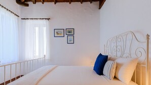 Een slaapkamer met een bed, witte gordijnen en twee foto's in lijsten aan de muur.