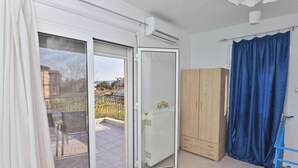 A room with a sliding glass door leading to an outdoor area, a radiator, a wooden wardrobe, and a blue curtain.