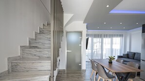 A modern interior with a marble staircase, a dining area with a wooden table and chairs, and a grey sofa. - Chryssis Village by Travel Pro Services - Nea Potidaia Halkidiki (Nea Potidaia)