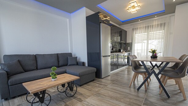 A modern living room with a sofa, coffee table, and dining area. - Chryssis Village by Travel Pro Services - Nea Potidaia Halkidiki (Nea Potidaia)