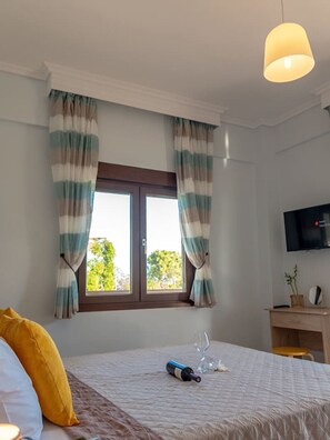 Ein Schlafzimmer mit Bett, Vorhängen, Fernseher, Schreibtisch und Fenster.