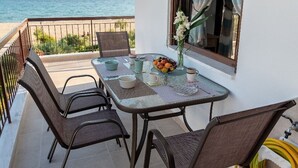 A balcony with a table set for four, chairs, a vase with flowers, and a view of the sea. - Dimi Seafront Αpartment by Rentals Pro (Nea Moudania)