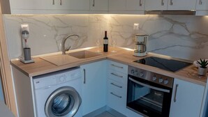 A compact kitchen with a washing machine, oven, and a coffee maker. - Dimi Seafront Αpartment by Rentals Pro (Nea Moudania)