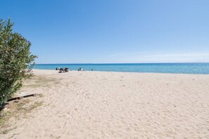 A sandy beach with a clear sky, a few people, and a stroller.
