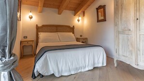 A bedroom with a wooden ceiling, a bed with white linens, two bedside tables, and a wardrobe. - Apartment 'Alpine Nest Loft' with Mountain View, Shared Pool and Wi-Fi (Pieve di Ledro)