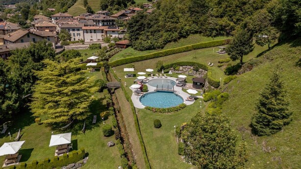 A hillside property with a swimming pool, lounge chairs, and a well-maintained garden. - Apartment 'Alpine Nest Loft' with Mountain View, Shared Pool and Wi-Fi (Pieve di Ledro)