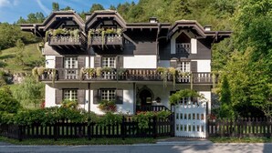 A two-story building with a balcony, a white picket fence, and greenery around. - Apartment 'Alpine Nest Loft' with Mountain View, Shared Pool and Wi-Fi (Pieve di Ledro)