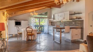 A spacious kitchen with modern appliances, a dining area with a round table and chairs, and a view through large windows. - Apartment 'Alpine Nest Loft' with Mountain View, Shared Pool and Wi-Fi (Pieve di Ledro)