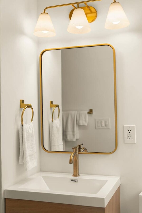 A bathroom with a white sink, gold fixtures, and three wall-mounted lights. - Newly Renovated Studio in Beachfront Building (Newport Beach)