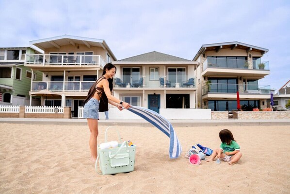 A beach scene with a woman and a child playing. There are houses in the background. - Remodeled 2-Bedroom Suite in Beachfront Building (Newport Beach)