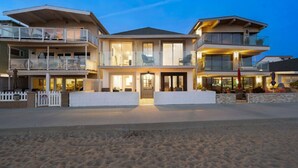 Um imóvel à beira-mar com uma casa de dois andares, um alpendre coberto e uma praia de areia em primeiro plano.