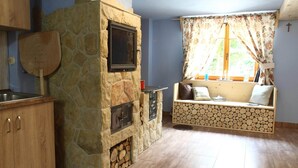 A stone fireplace with a TV, wooden cabinets, a log bench, and a window with curtains. - Cosy Apartment in Lapsze Nizne With Sauna (Lapsze Nizne)