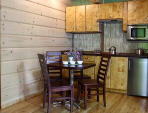 Interior de madera con una mesa de comedor, sillas, una zona de cocina con microondas y un refrigerador.