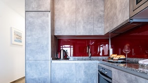 Une cuisine moderne avec des meubles gris, un pare-feu rouge et une bouilloire en acier inoxydable posée sur le plan de travail.