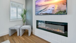 Ein modernes Wohnzimmer mit Kamin, großem Wandfernseher und einem Fenster mit Jalousien.