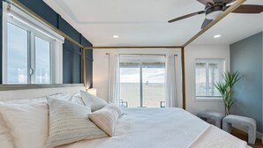 Ein Schlafzimmer mit einem großen Bett, einem Deckenventilator, Blick auf den Strand und einem Fenster mit Vorhängen.