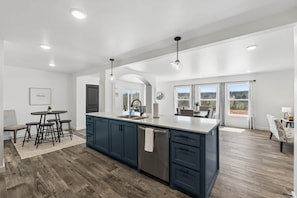 A modern kitchen with a large island, dark blue cabinets, and a view to the outside. - NEW! Ball Field House at All Star Sports Village (Choctaw)