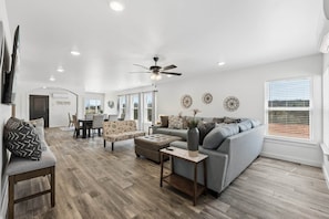 A spacious living room with a gray sofa, a wooden coffee table, and a ceiling fan. - NEW! Ball Field House at All Star Sports Village (Choctaw)