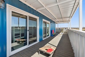 A covered deck with a blue building, sliding glass doors, and outdoor furniture. - NEW! Ball Field House at All Star Sports Village (Choctaw)