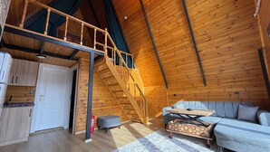 A wooden interior with a loft bedroom, a sofa, a table, and a kitchen area. - Kumsal bungalov (Ondokuzmayis)