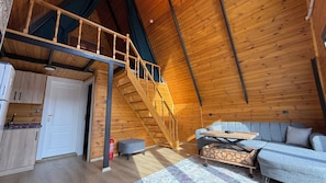 A wooden interior with a loft bedroom, a sofa, a table, and a kitchen area. - Kumsal bungalov (Ondokuzmayis)