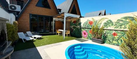 A modern house with a swimming pool, a patio with lounge chairs, and a mural of tropical plants.