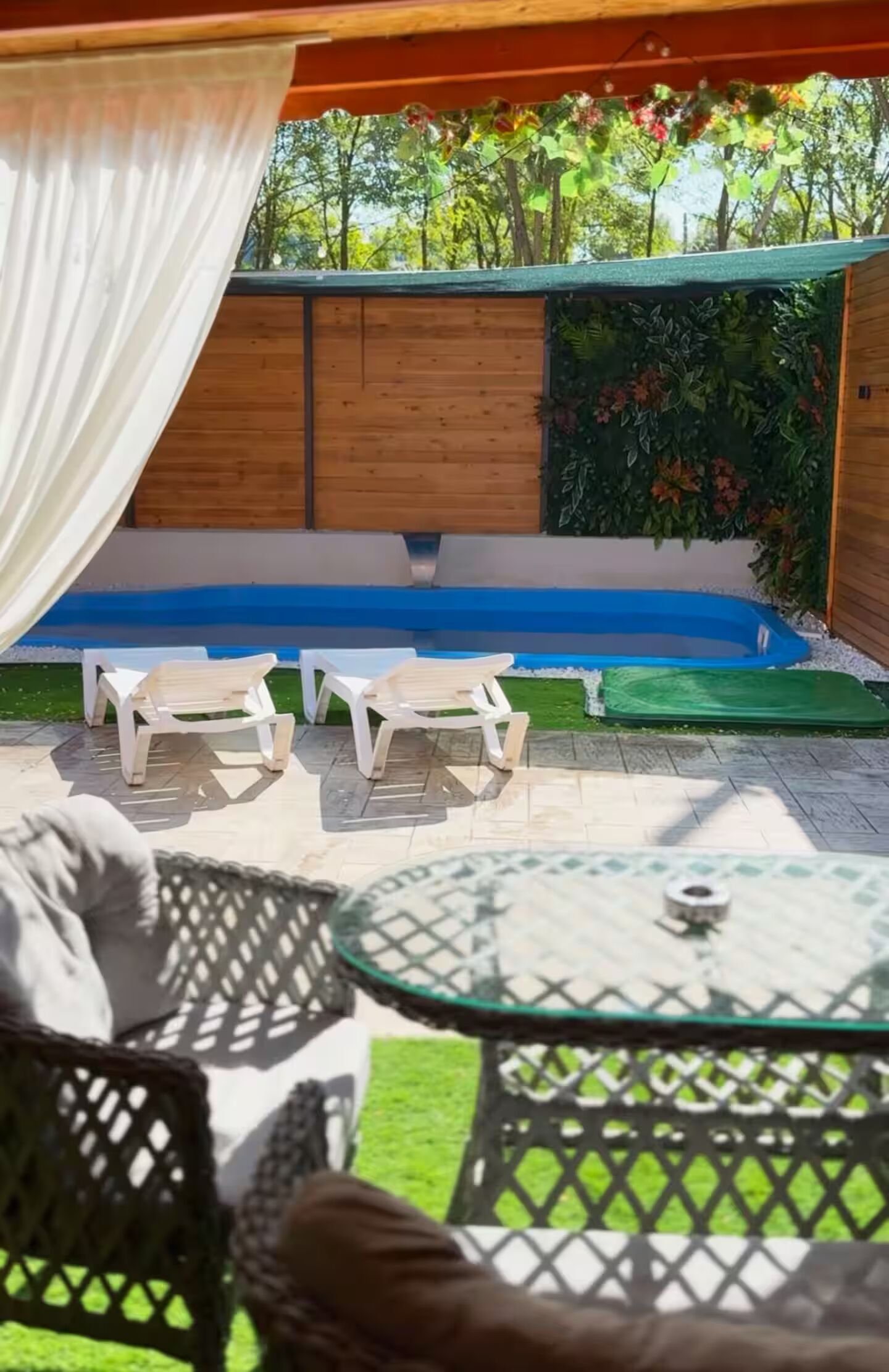 An outdoor seating area with a pool, a wooden deck, and a green lawn.