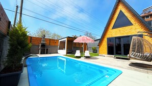 A backyard with a swimming pool, a barbecue area, and a wooden house with a triangular roof. - Kumsal bungalov (Ondokuzmayis)