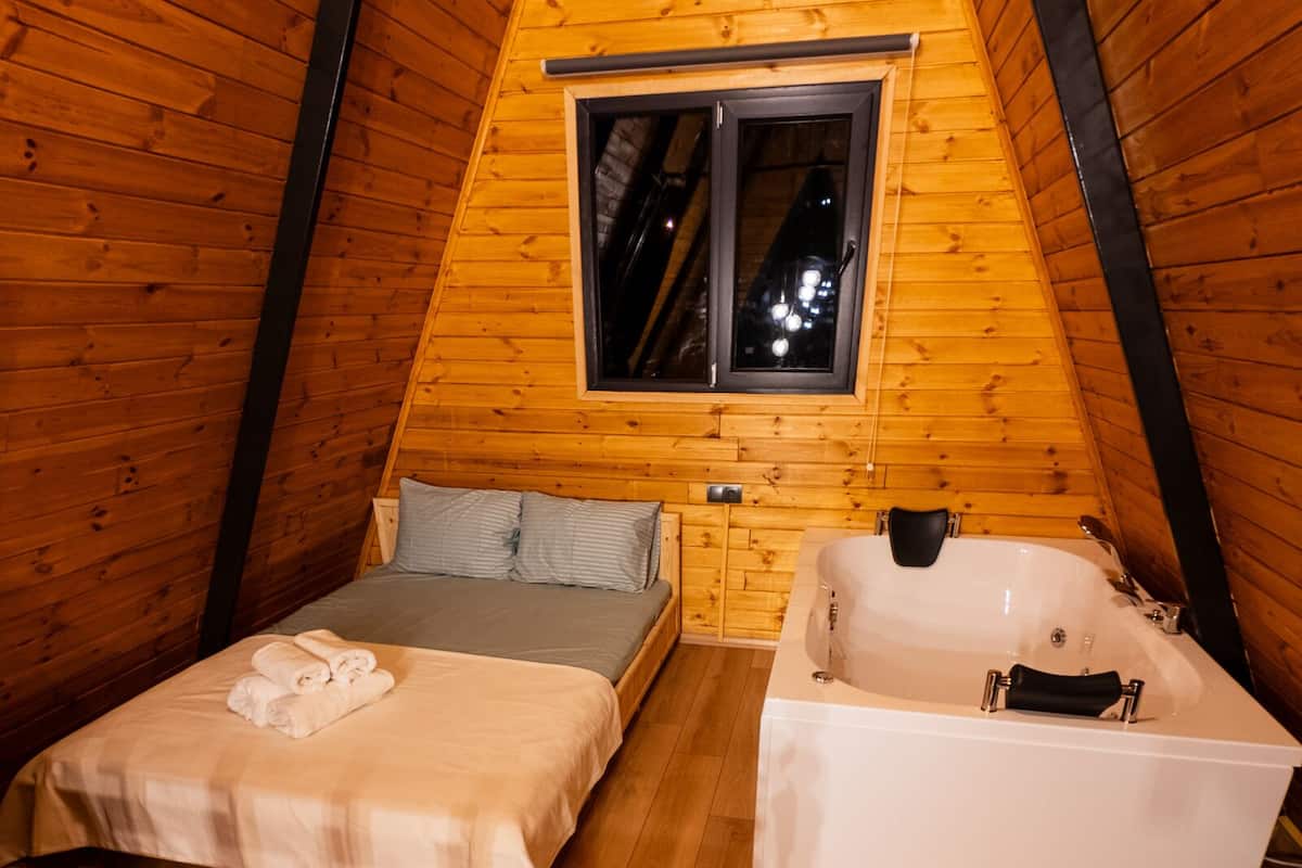 A cozy, triangular wooden room with a bed, a bench, and a bathtub.